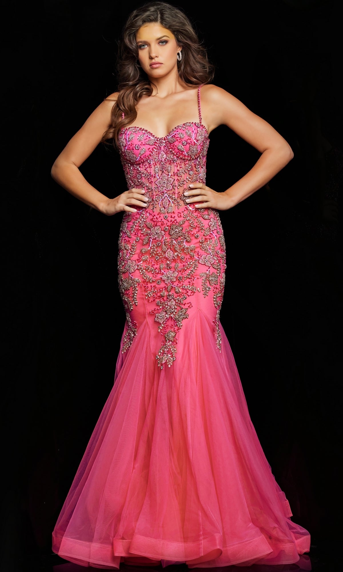 A woman wears the Jovani Beaded Sheer-Bodice Long Prom Dress 23125, a bright pink gown with intricate embellishments, standing against a black background.